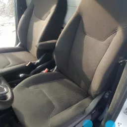 Dwa czarne fotele samochodowe z tapicerką w delikatny wzór kropek, widoczne z perspektywy kierowcy, z logo firmy czyszczącej w prawym dolnym rogu.