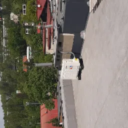 Biała jednostka zewnętrzna klimatyzacji zamontowana na płaskim dachu budynku z widokiem na okoliczną zabudowę i zieleń.