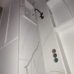 Nowoczesna łazienka w trakcie wykańczania, z marmurową ścianą, wnęką z umywalką i widocznymi instalacjami wodnymi.