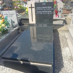 K2 STONE Kamieniarstwo Chruślicki - Czarny, polerowany nagrobek z wygrawerowanym krzyżem i inskrypcjami na cmentarzu, otoczony jasnym żwirem i innymi nagrobkami w tle.