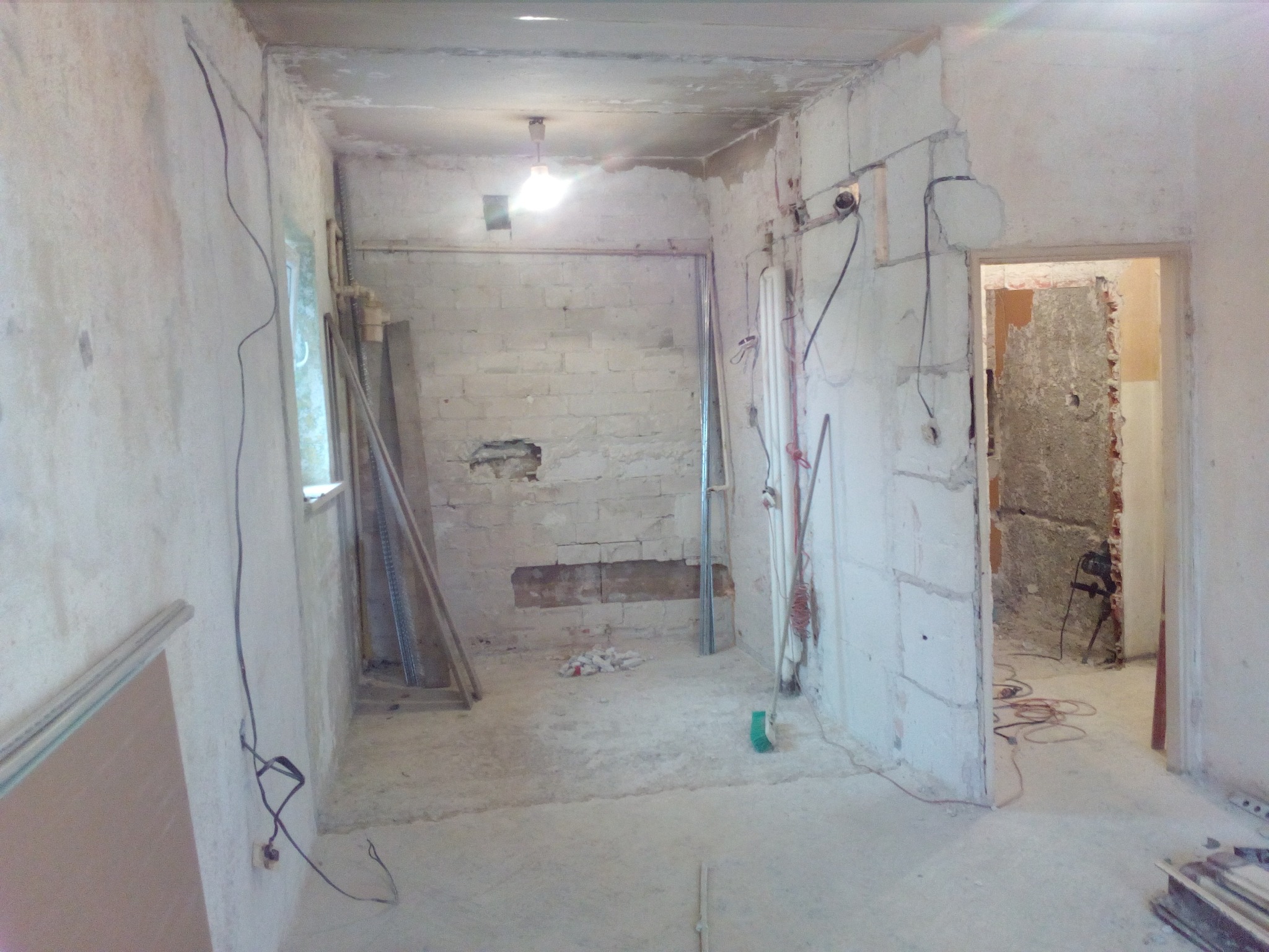 Wnętrze pokoju przed remontem: surowe ściany z cegieł i betonu, widoczne kable elektryczne, brak wykończenia, przygotowane do dalszych prac.