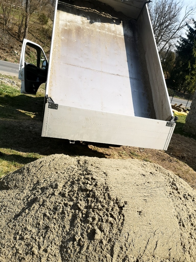 Wyładowana pospółka z wywrotki na trawniku, widoczna otwarta kabina pojazdu.