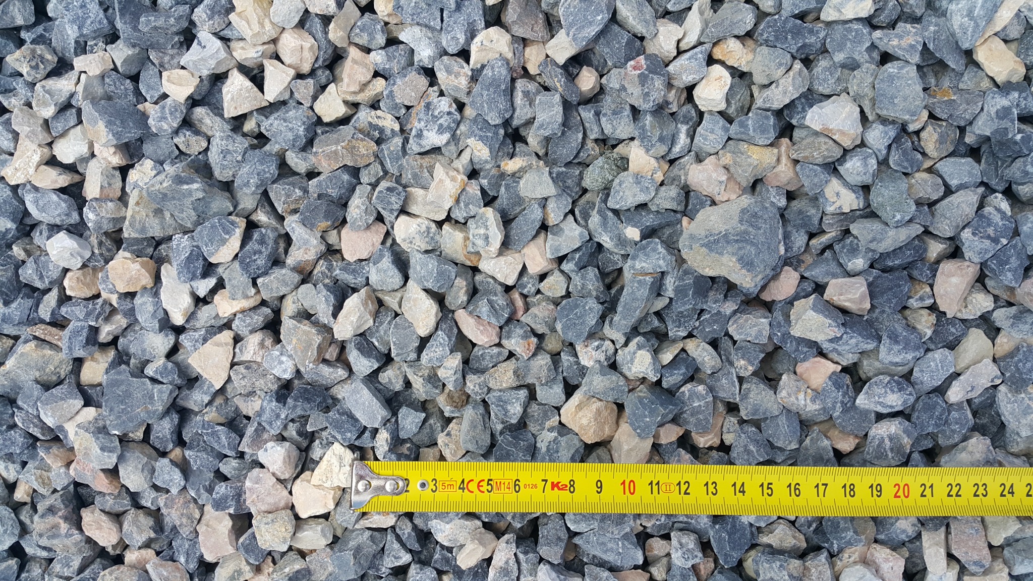 Szaro-beżowy kamień ozdobny o frakcji mierzonej żółtą taśmą mierniczą, widok z góry.