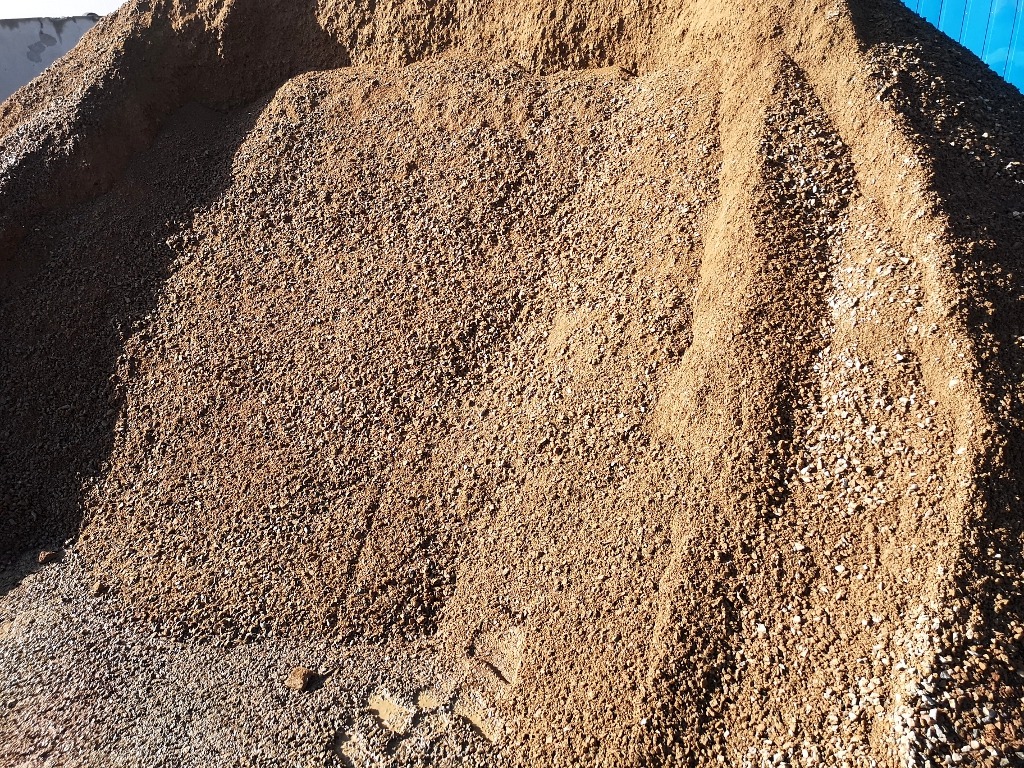 Kupa piasku z domieszką żwiru, widoczne ślady opon na ziemi, jasne oświetlenie.