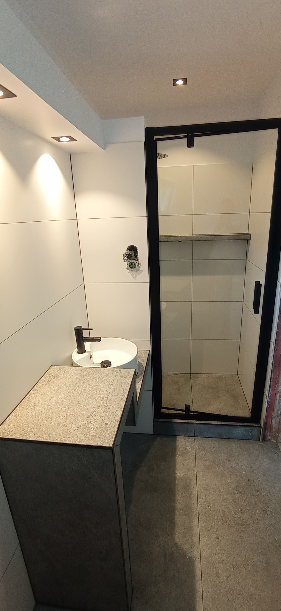 Nowoczesna łazienka z kabiną prysznicową z czarną ramą, okrągłą umywalką nablatową i blatem z szarego kamienia.