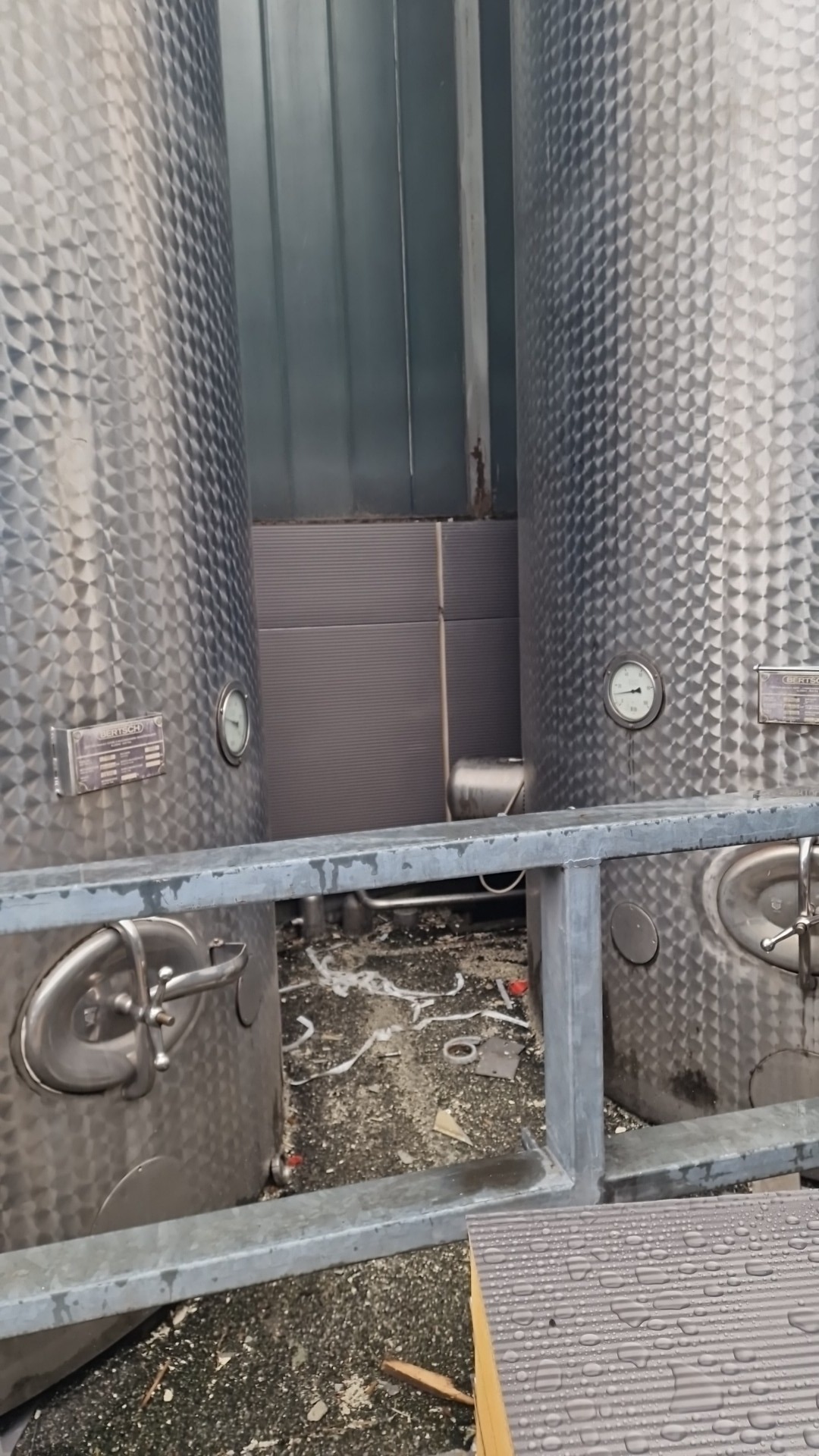 Dwa stalowe zbiorniki przemysłowe z manometrami i zaworami, widoczne ślady montażu i drobne zanieczyszczenia na podłożu, fragment stalowej konstrukcji ramowej na pierwszym planie.