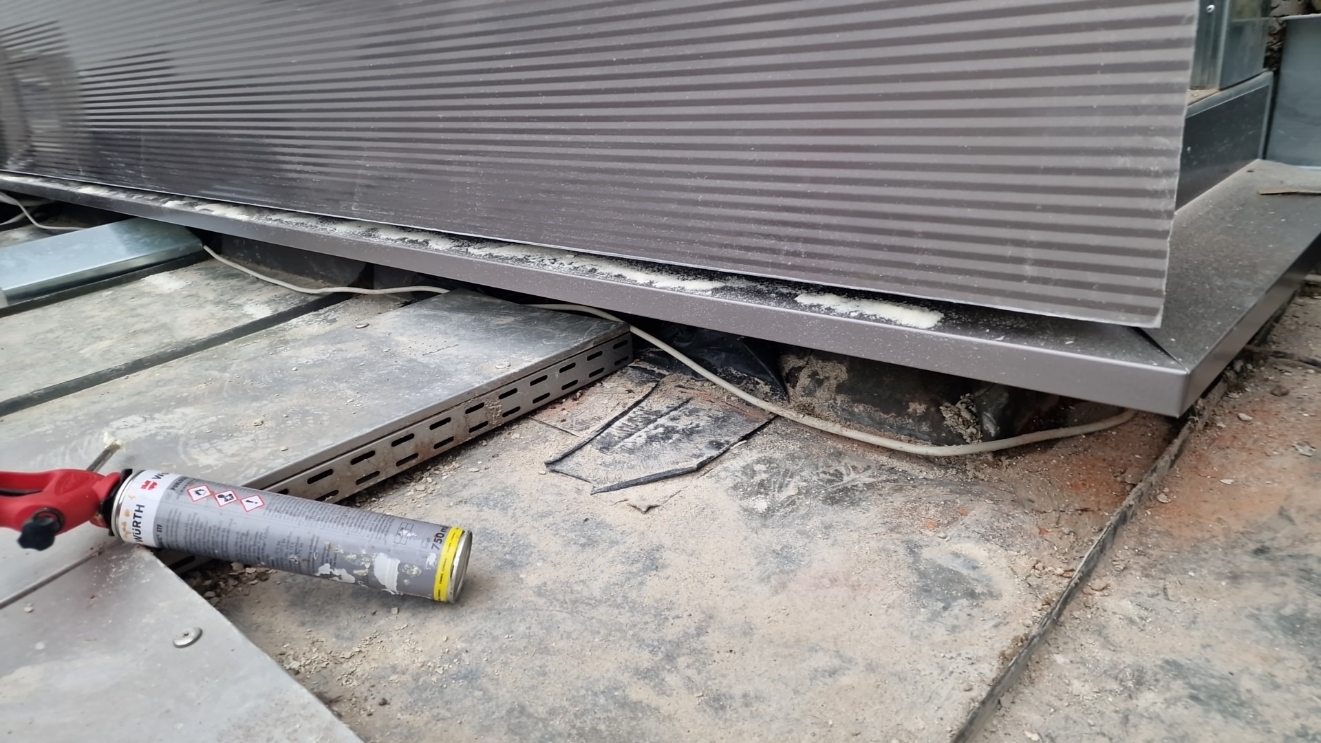 Detale montażu płyty warstwowej: widoczna szczelina wypełniona pianką montażową, przewód i narzędzie do aplikacji pianki Wurth.