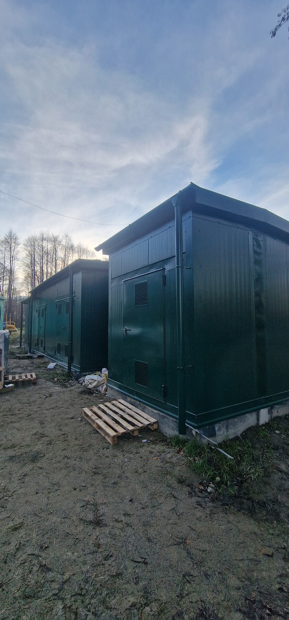 Dwa zielone, stalowe kontenery w Rybniku, ustawione obok siebie na ziemi, z widocznymi paletami drewnianymi z przodu. Kontenery posiadają drzwi i kratki wentylacyjne.