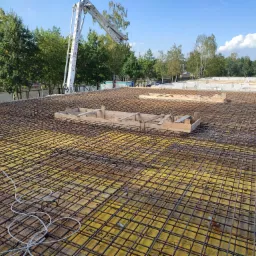 Zbrojenie płyty fundamentowej z deskowaniem w Warszawie, widoczna pompa do betonu w tle.