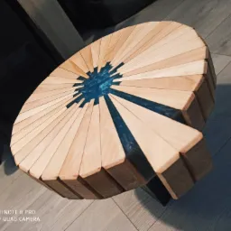 Okrągły stolik kawowy z drewnianych klinów i żywicy epoksydowej w kolorze błękitu, widoczny na podłodze z paneli.