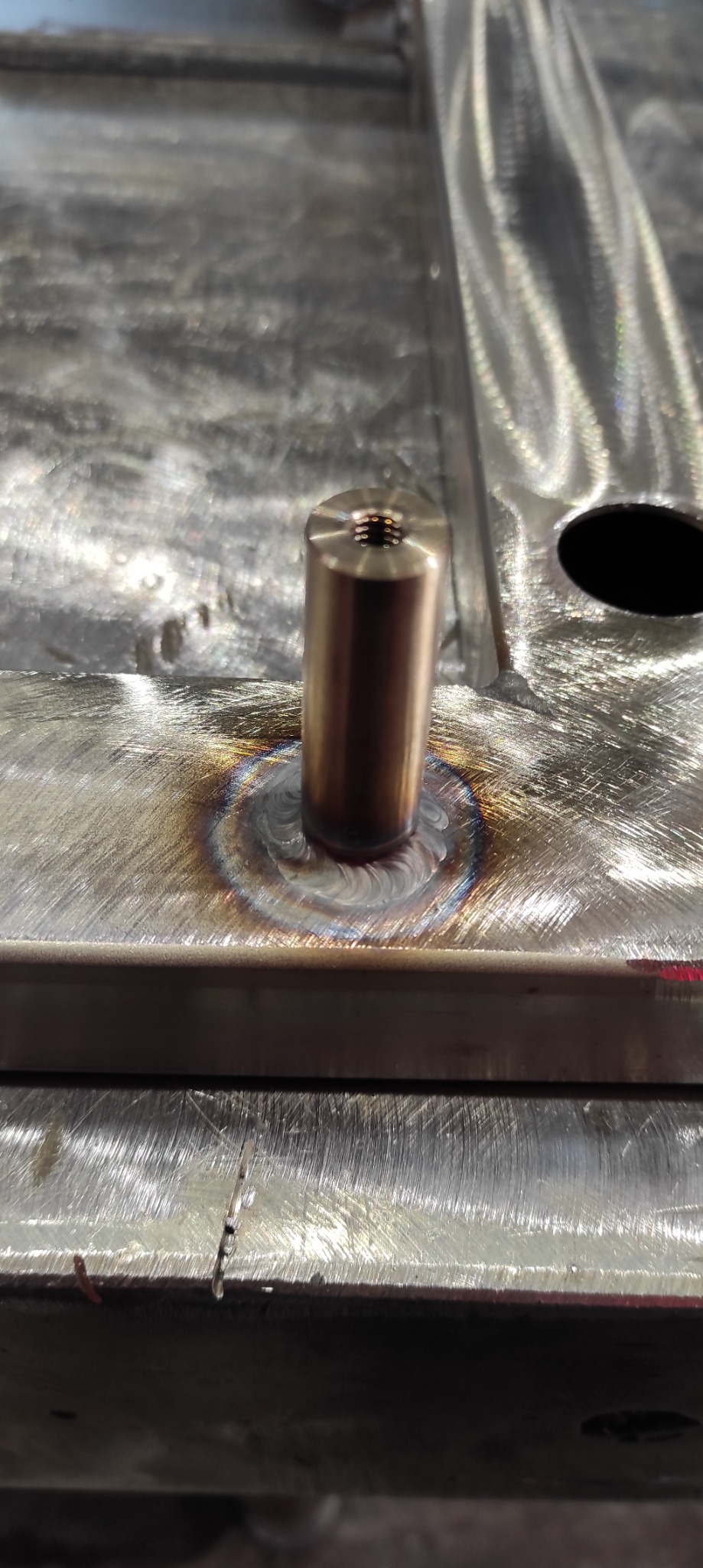 Metalowa podstawa z przyspawanym, mosiężnym elementem cylindrycznym z gwintem wewnętrznym, widoczne ślady spawania i obróbki.