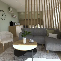 Wnętrze mieszkania z szarą sofą narożną, okrągłym stolikiem kawowym z rośliną i filiżanką, beżowym fotelem oraz otwartą kuchnią w tle, oddzielone drewnianą ażurową ścianką.