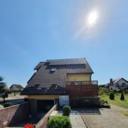 Instalacja paneli słonecznych na dachu domu jednorodzinnego w Łubianie, orientacja wschód-zachód, widok z podjazdu w słoneczny dzień.
