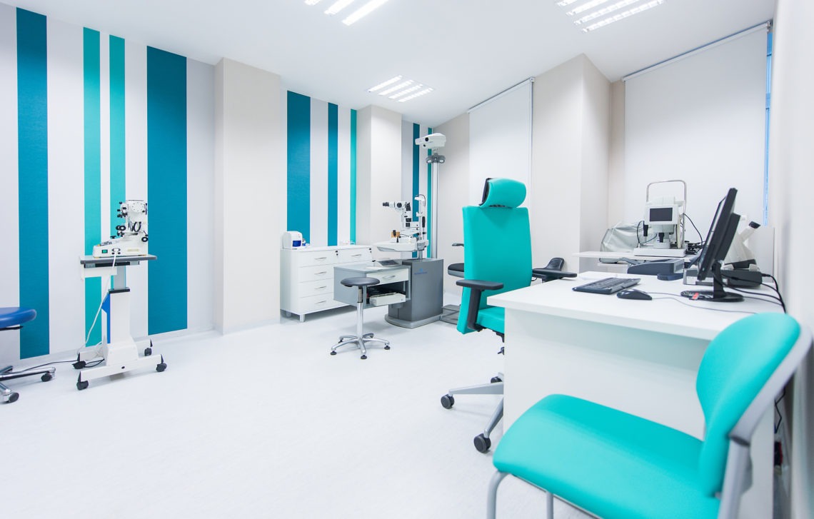 Jasne, minimalistyczne wnętrze gabinetu lekarskiego z nowoczesnym sprzętem diagnostycznym, turkusowymi akcentami na ścianach i krzesłach, oraz białymi meblami i podłogą.