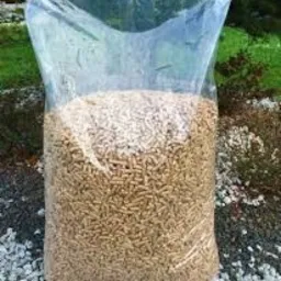 Wypełniony przezroczysty worek z granulatem opałowym na tle żwirowego podłoża i zieleni ogrodowej.