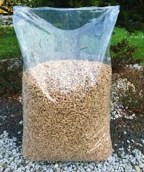 Wypełniony przezroczysty worek z granulatem opałowym na tle żwirowego podłoża i zieleni ogrodowej.