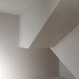 Świeżo położona, jasna, gładka warstwa na ścianach i suficie w pomieszczeniu ze skosami, widoczny kabel przy podłodze.