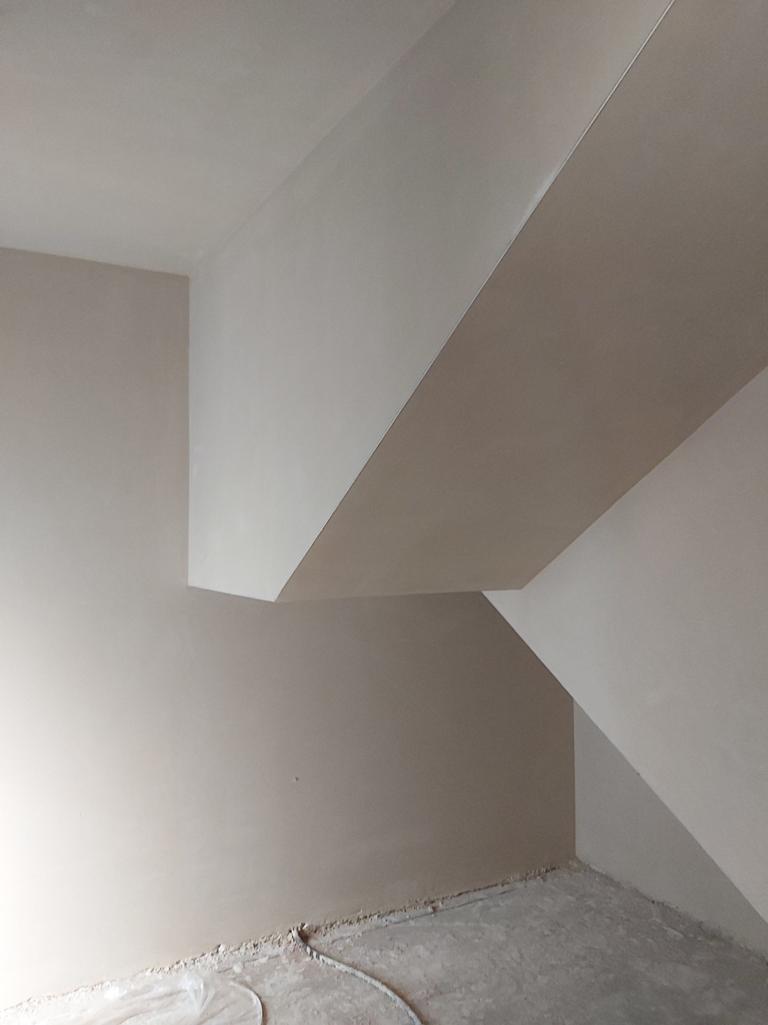 Świeżo położona, jasna, gładka warstwa na ścianach i suficie w pomieszczeniu ze skosami, widoczny kabel przy podłodze.