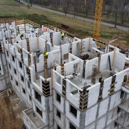 FIRWIT-SERVICE SPÓŁKA Z OGRANICZONĄ ODPOWIEDZIALNOŚCIĄ SPÓŁKA KOMANDYTOWA - Wysoki budynek w trakcie budowy z betonu komórkowego, widok z góry. Żuraw budowlany w tle. Pracownicy w kamizelkach odblaskowych na budowie.