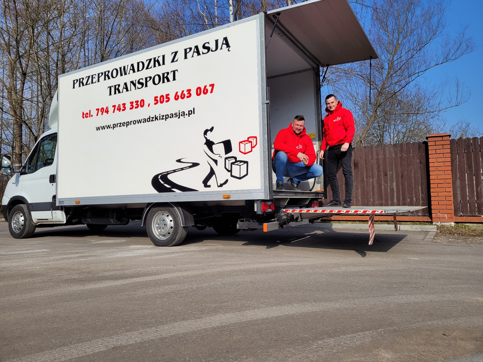 Biały samochód dostawczy z otwartą przestrzenią ładunkową na zewnątrz, z grafiką przedstawiającą sylwetkę osoby niosącej kartony i napisem 'Przeprowadzki z pasją Transport' oraz dwoma mężczyznami...