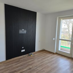 MALINIAK.pl - Pokój z panelami ściennymi z czarnych listew, przygotowany do montażu telewizora, widoczne gniazdka elektryczne i przewody.
