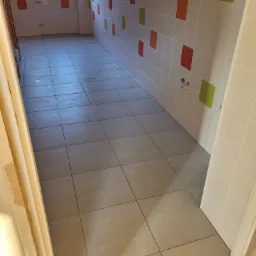 Ukończona łazienka z szarymi płytkami podłogowymi i białymi płytkami ściennymi z czerwonymi i zielonymi akcentami, widoczne przyłącza wodne.