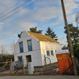 Ag-bud Agnieszka Mikołajczyk - Dom w trakcie budowy z widoczną konstrukcją dachu, styropianem na elewacji i przenośną toaletą WC Skip na posesji.