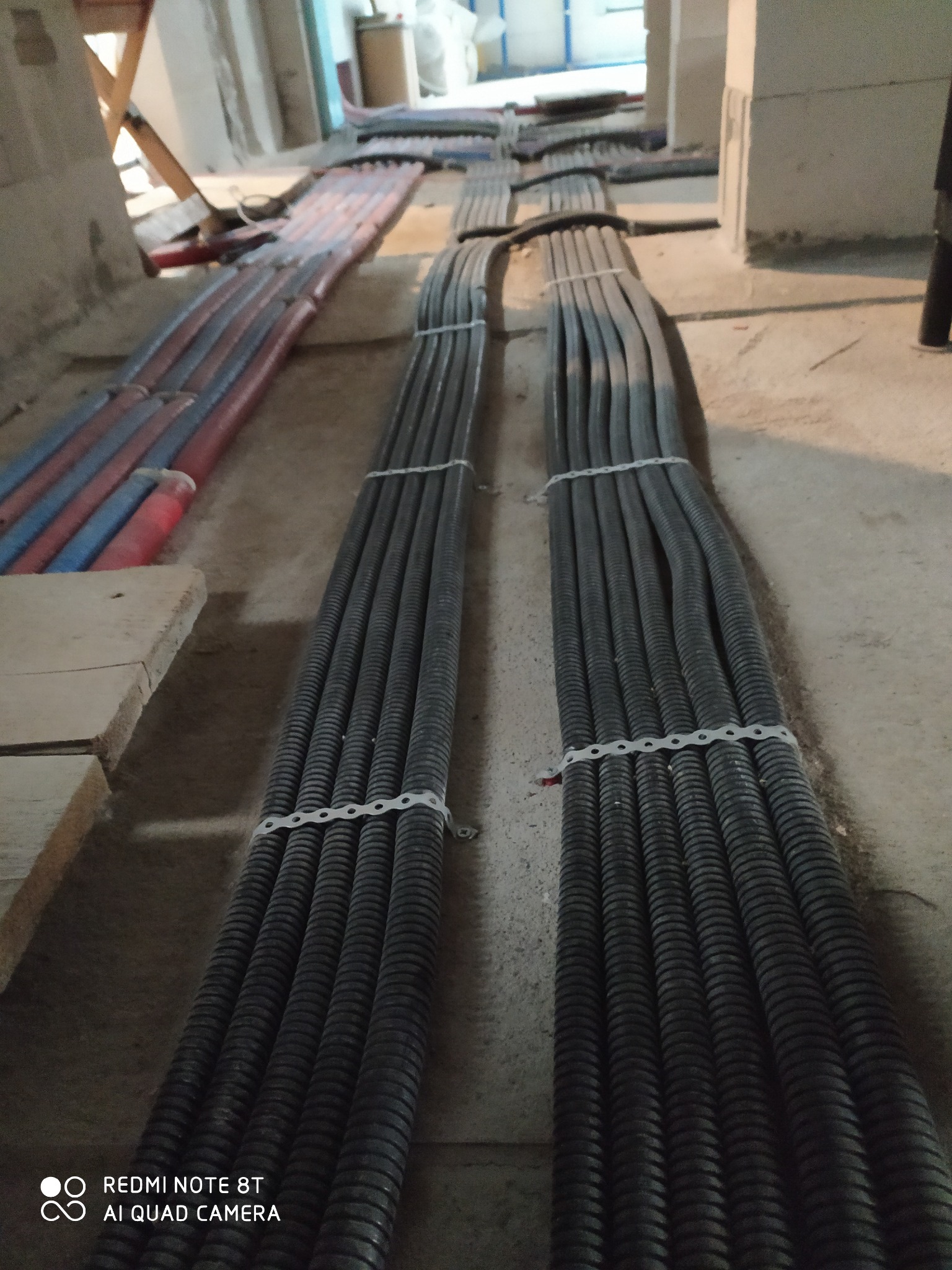 Rzędy czarnych i czerwono-niebieskich rur instalacyjnych, ułożone wzdłuż surowego betonowego podłoża w trakcie prac instalacyjnych w budynku w stanie deweloperskim.