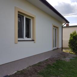 Remonty Patryk Nowakowski - Elewacja domu jednorodzinnego po remoncie, widoczne ocieplenie ścian i odmalowane okna z kremowymi ramami, jasna elewacja i ciemniejsza podmurówka.