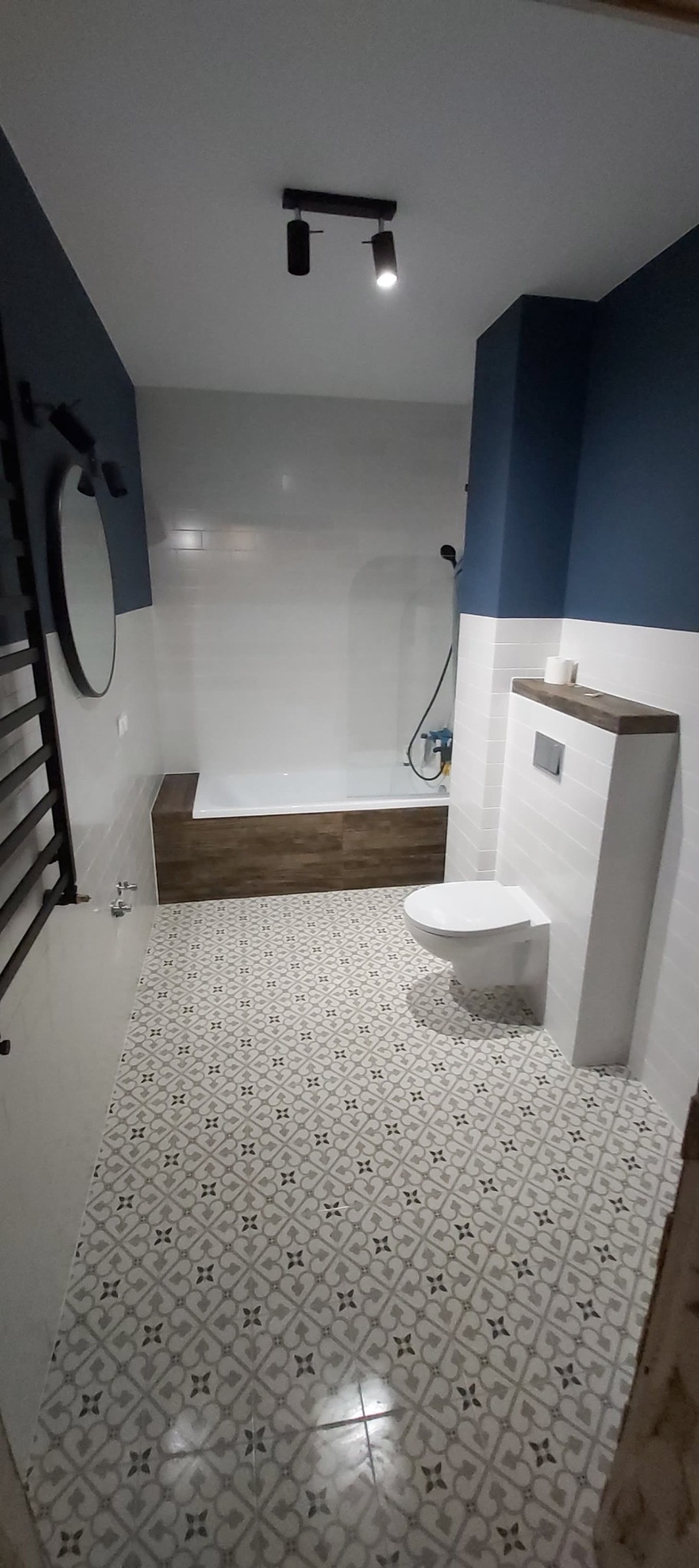 Nowoczesna łazienka z biało-granatowymi ścianami, wzorzystą szaro-białą podłogą, podwieszaną toaletą i grzejnikiem drabinkowym