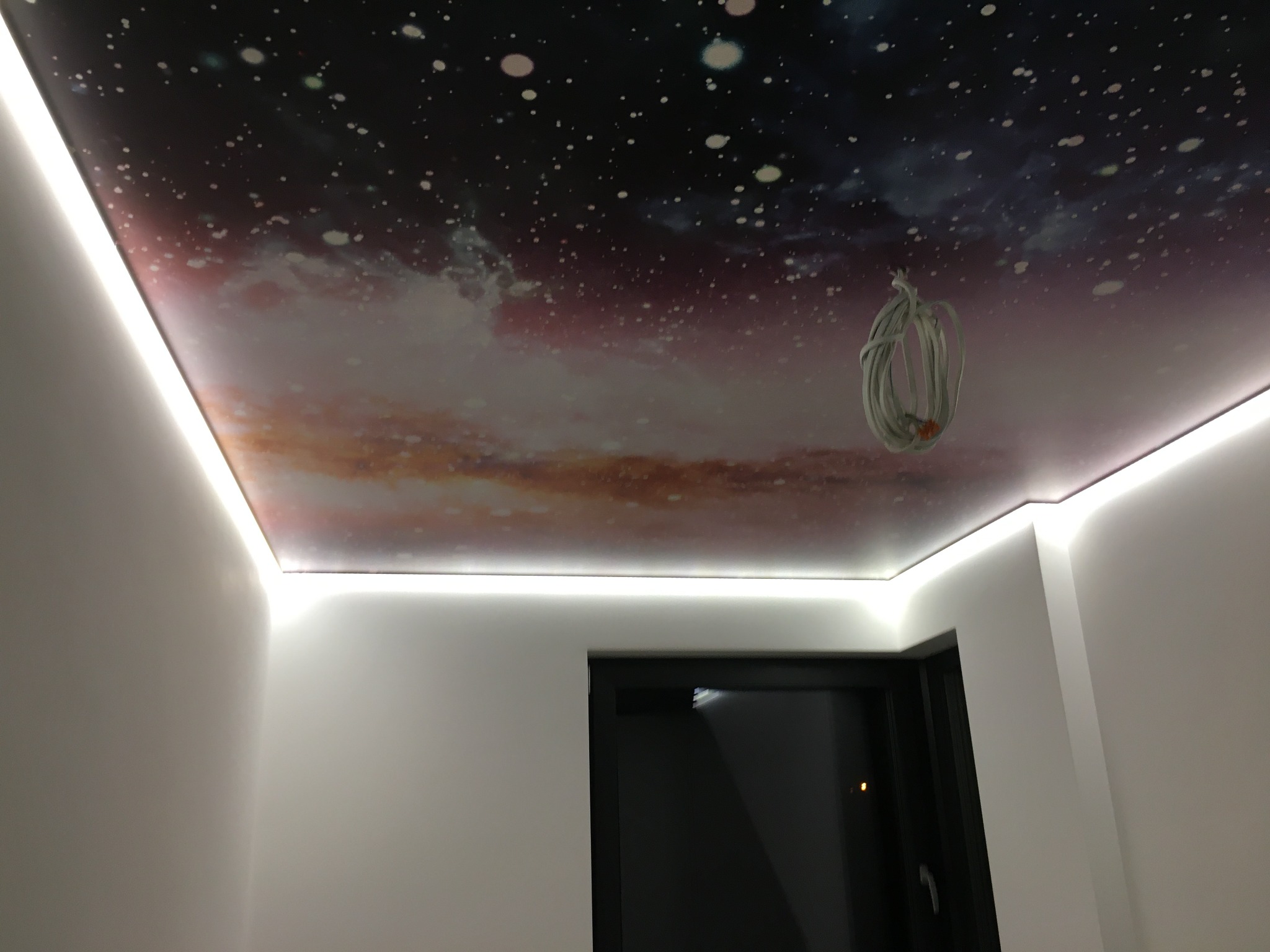 Nowoczesny sufit z podświetleniem LED i motywem kosmosu, widoczne zwisające kable przed finalnym wykończeniem.