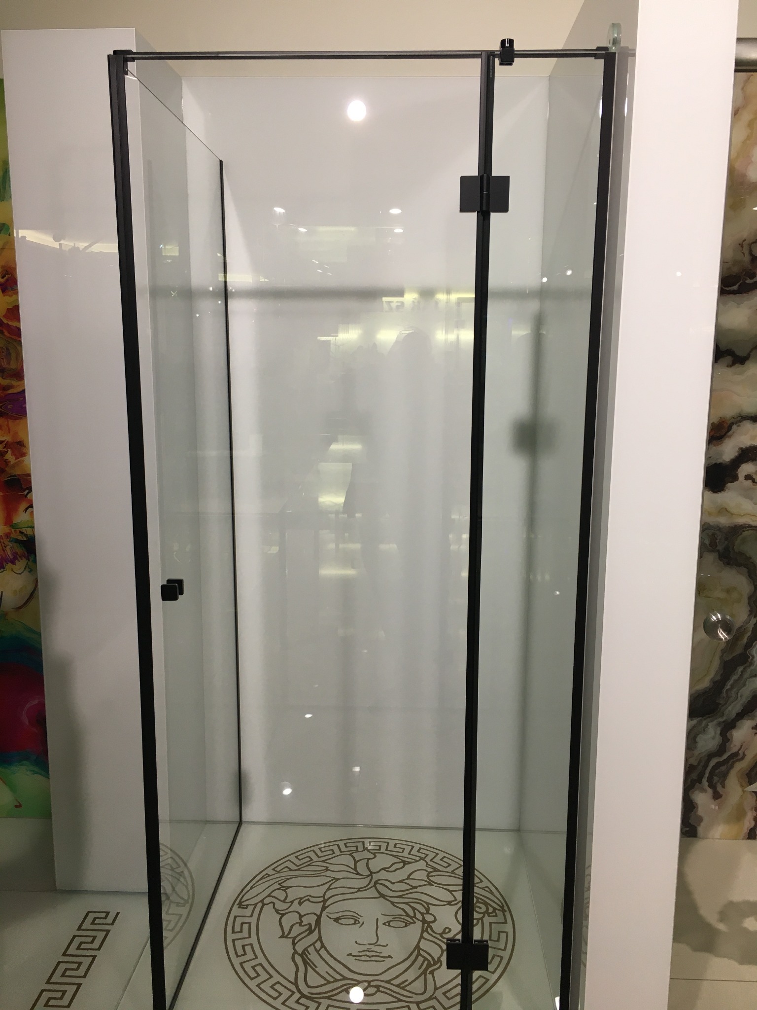 Kabina prysznicowa z czarnymi profilami i szklanymi drzwiami, widoczna dekoracyjna podłoga z motywem głowy Meduzy.