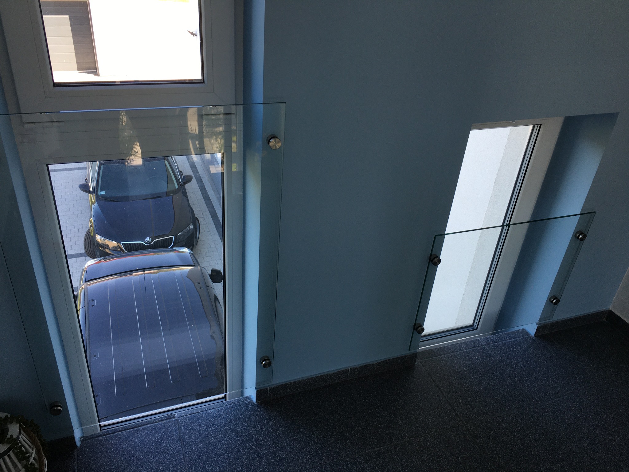 Szklana balustrada wewnętrzna z mocowaniem punktowym, widok z góry na dwa samochody zaparkowane na zewnątrz.