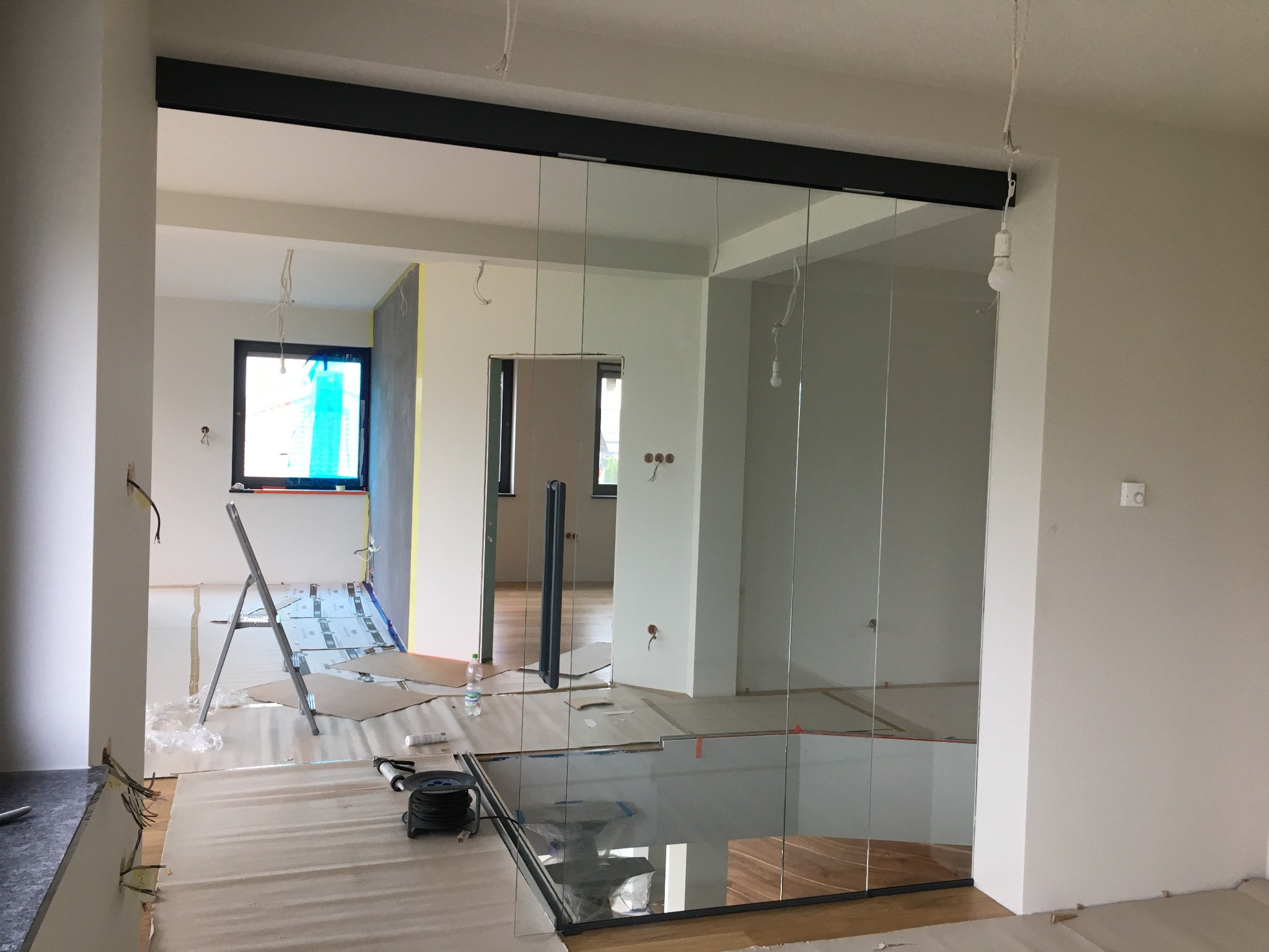 Montaż szklanych drzwi przesuwnych w trakcie wykańczania wnętrza, widoczne zabezpieczenia podłogi i ściany, drabina malarska w tle.