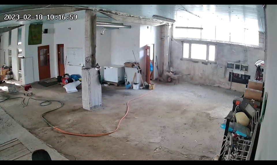 Wnętrze remontowanego magazynu z widocznymi przewodami, narzędziami i materiałami budowlanymi, surowe ściany i podłoga w trakcie prac wykończeniowych.