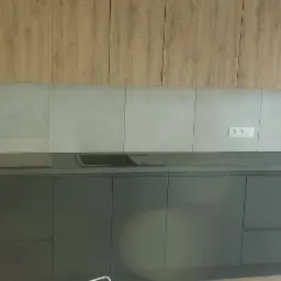 Nowoczesna kuchnia z szarymi szafkami dolnymi, drewnopodobnymi górnymi, szarymi płytkami na ścianie, czarnym blatem i minimalistycznym zlewem.