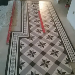 Układanie wzorzystych, szaro-białych płytek podłogowych w korytarzu, widoczny poziomica i krzyżyki dystansowe.