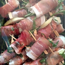 Bemiko - Eleganckie koreczki z szynki parmeńskiej i melona na rukoli, podane w czarnym, plastikowym pojemniku cateringowym. Idealne na imprezę firmową lub przyjęcie świąteczne.