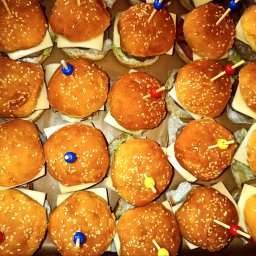 Bemiko - Mini burgery z serem i kolorowymi wykałaczkami, ułożone w rzędach. Widok z góry, ciepłe światło podkreśla złocisty kolor bułek posypanych sezamem.