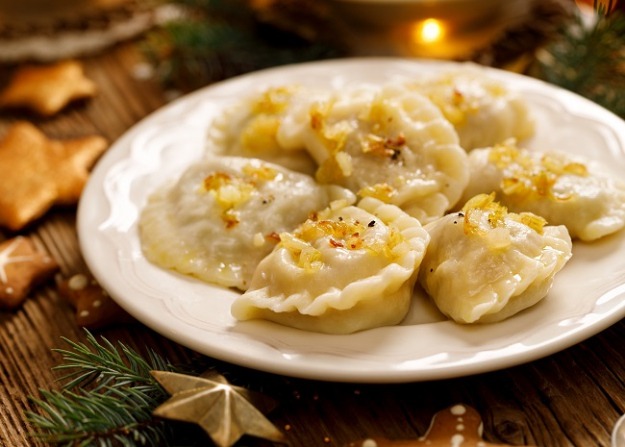 Świąteczne pierogi z kapustą i grzybami na białym talerzu, udekorowane gałązką świerku i piernikami. Ciepłe światło świec w tle tworzy przytulną atmosferę.