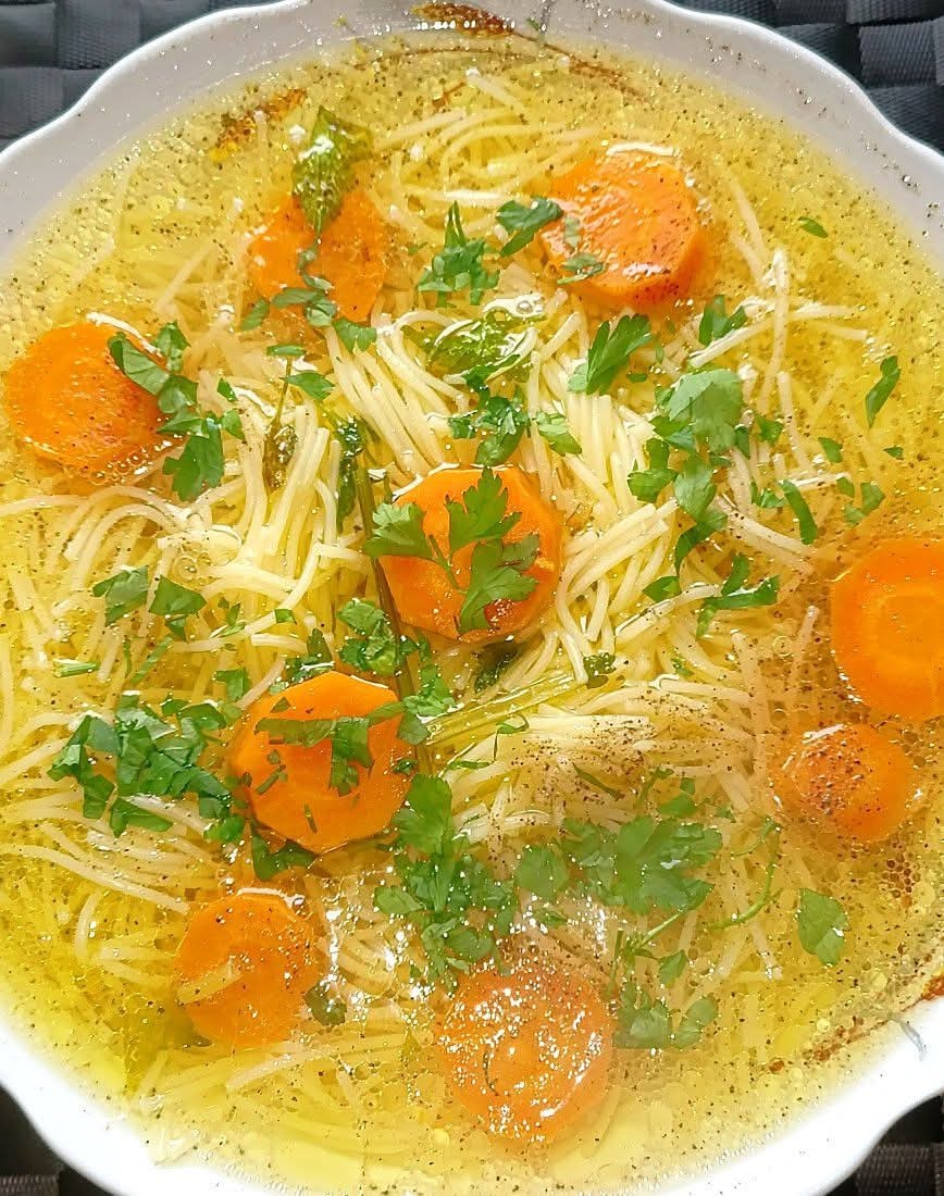 Aromatyczny rosół z makaronem i marchewką, udekorowany świeżą natką pietruszki, podany w białym talerzu. Delikatne oświetlenie podkreśla klarowność bulionu.