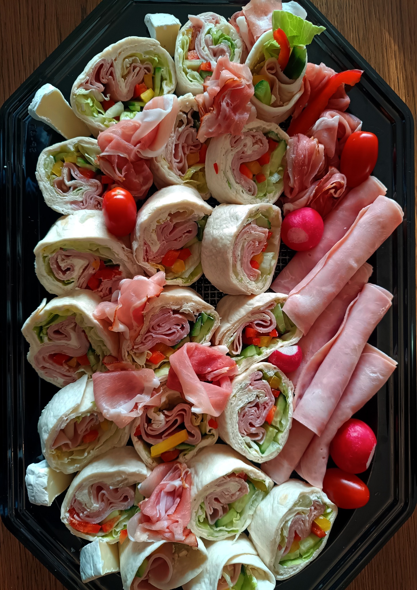 Elegancka taca z roladkami tortilli z szynką, warzywami i serem brie, uzupełniona szynką parmeńską, rzodkiewkami i pomidorkami koktajlowymi. Idealna na catering.