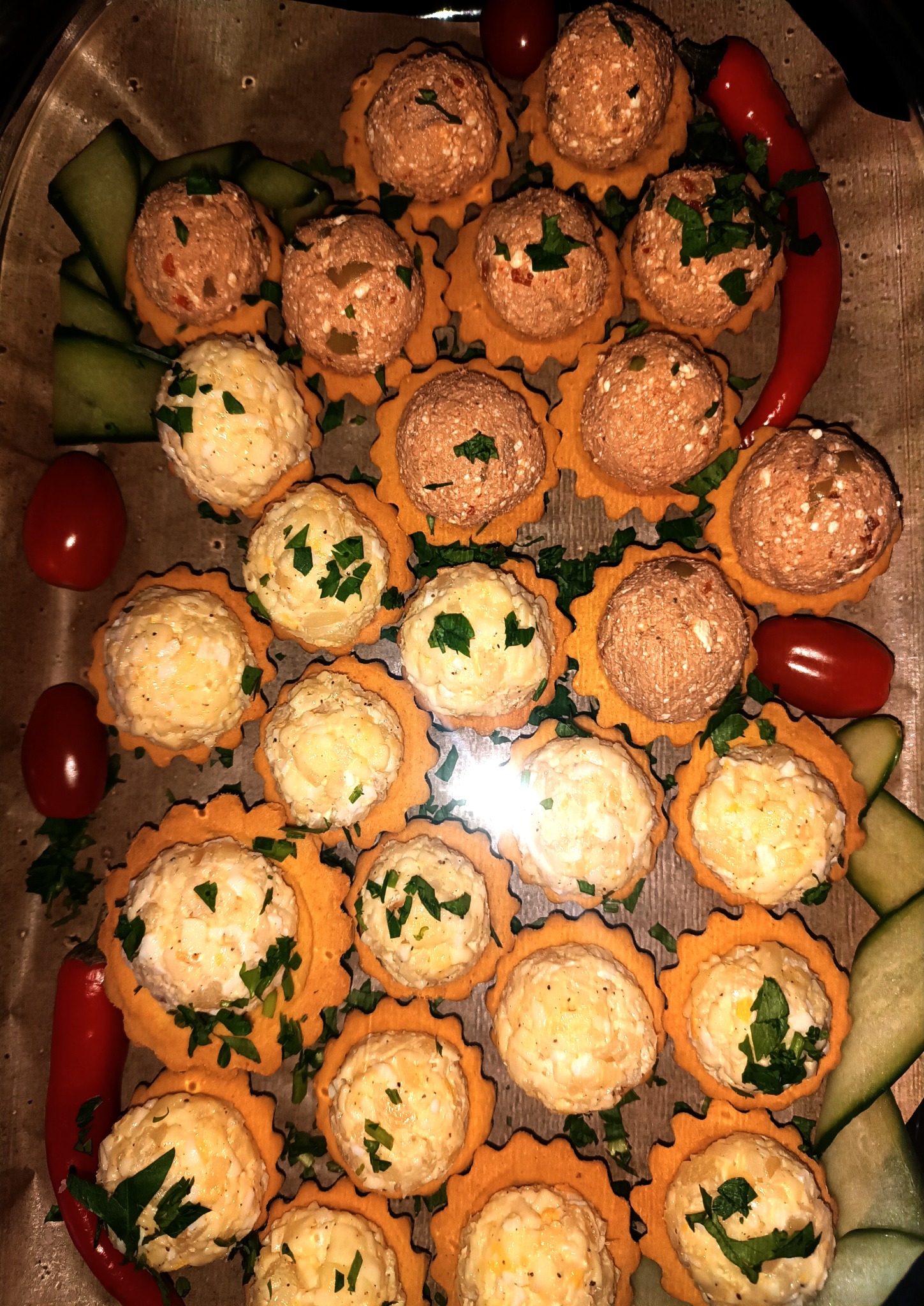 Dekoracyjne tartaletki z pastami, posypane zieloną pietruszką, ułożone na tacy z dodatkiem ogórka, pomidorów i papryki chili. Różne smaki past.