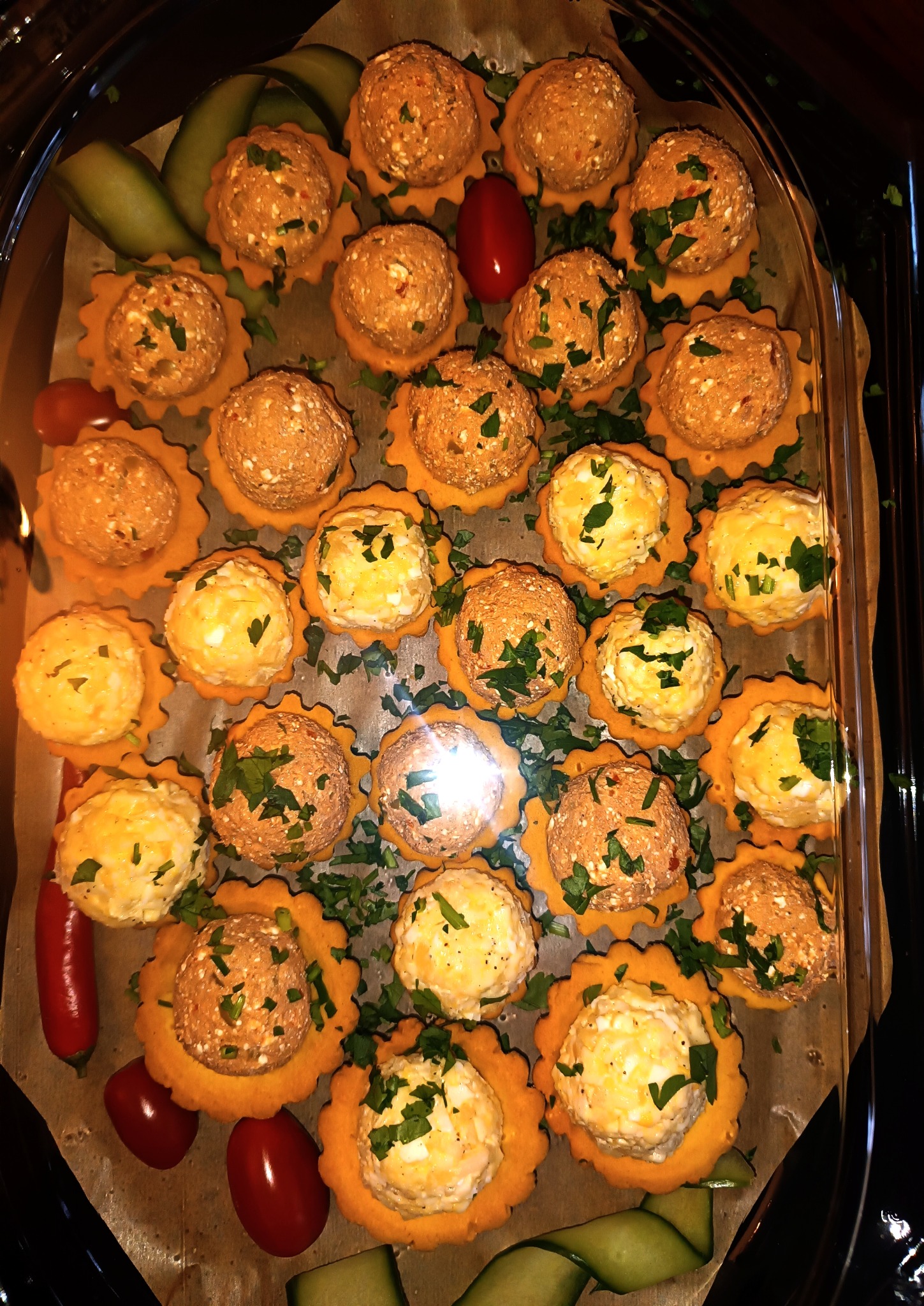 Dekoracyjne tartaletki z kulkami pasty, posypane zieloną pietruszką, ułożone na tacy z plastrami ogórka i pomidorkami koktajlowymi. Różne kolory past.