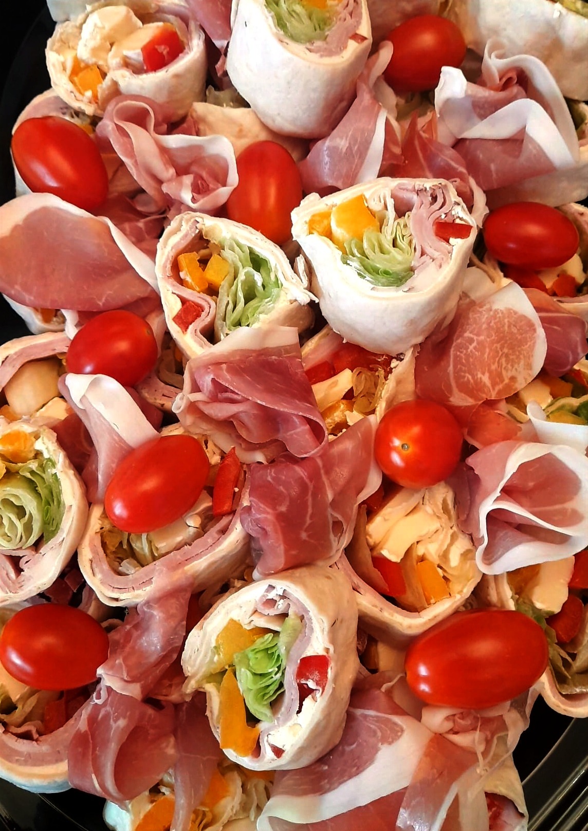 Tortilla wrap rolls with ham, lettuce, peppers, and tomatoes, arranged on a platter. Close-up shot showcasing fresh ingredients and vibrant colors.