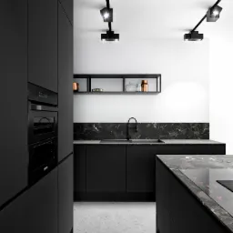 Nowoczesna, minimalistyczna kuchnia w czarnych matowych odcieniach z marmurowym blatem i oświetleniem punktowym na szynoprzewodzie.