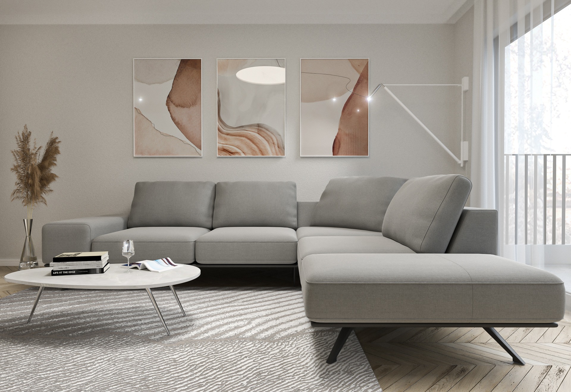 Jasnoszara sofa narożna z podnóżkiem, stolik kawowy z książkami i szklanką, trzy abstrakcyjne obrazy na ścianie, lampa podłogowa, dywan w geometryczny wzór, parkiet