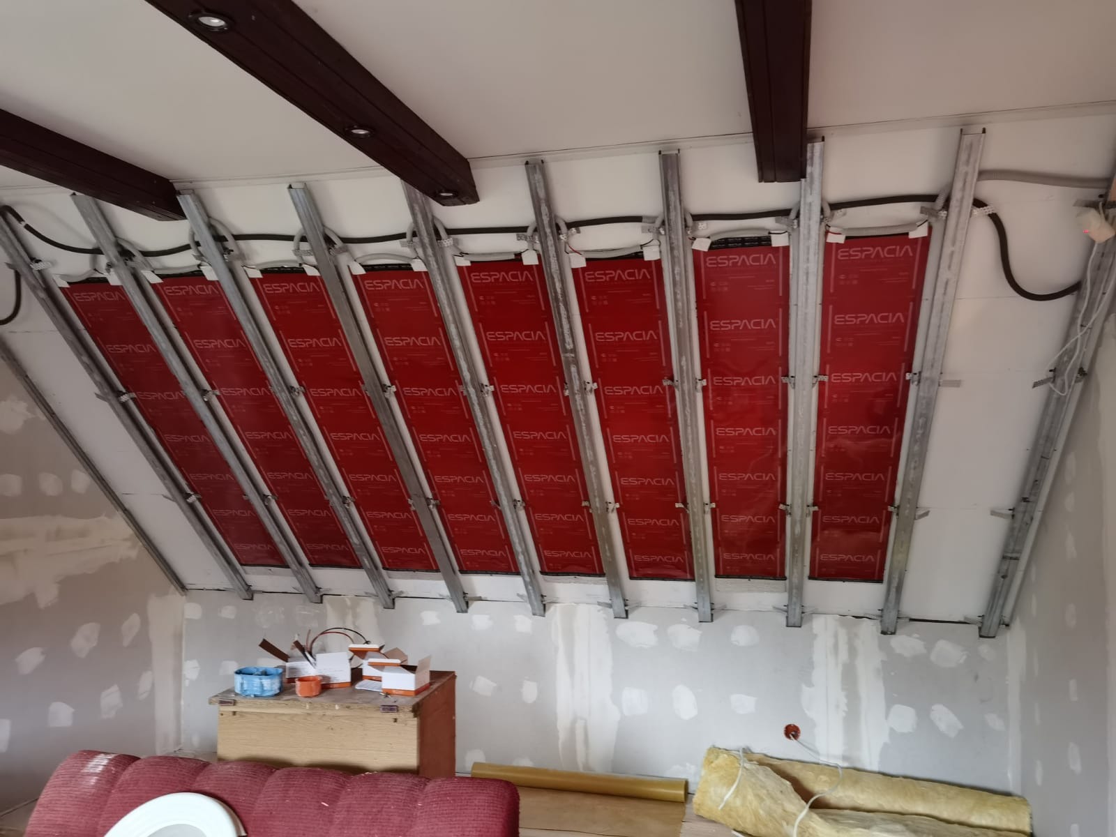 Montaż czerwonych mat grzewczych ESPACIA na poddaszu w Kórniku, widoczne metalowe profile i przewody elektryczne przed wykończeniem ścian.