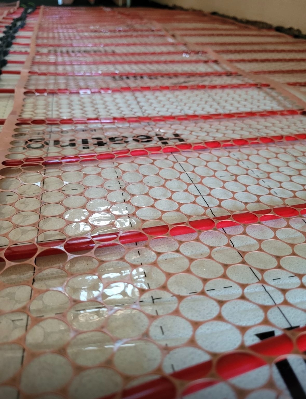 Rozłożona mata grzewcza z czerwonymi przewodami na podłodze z zaznaczonymi liniami pomocniczymi przed zalaniem wylewką.