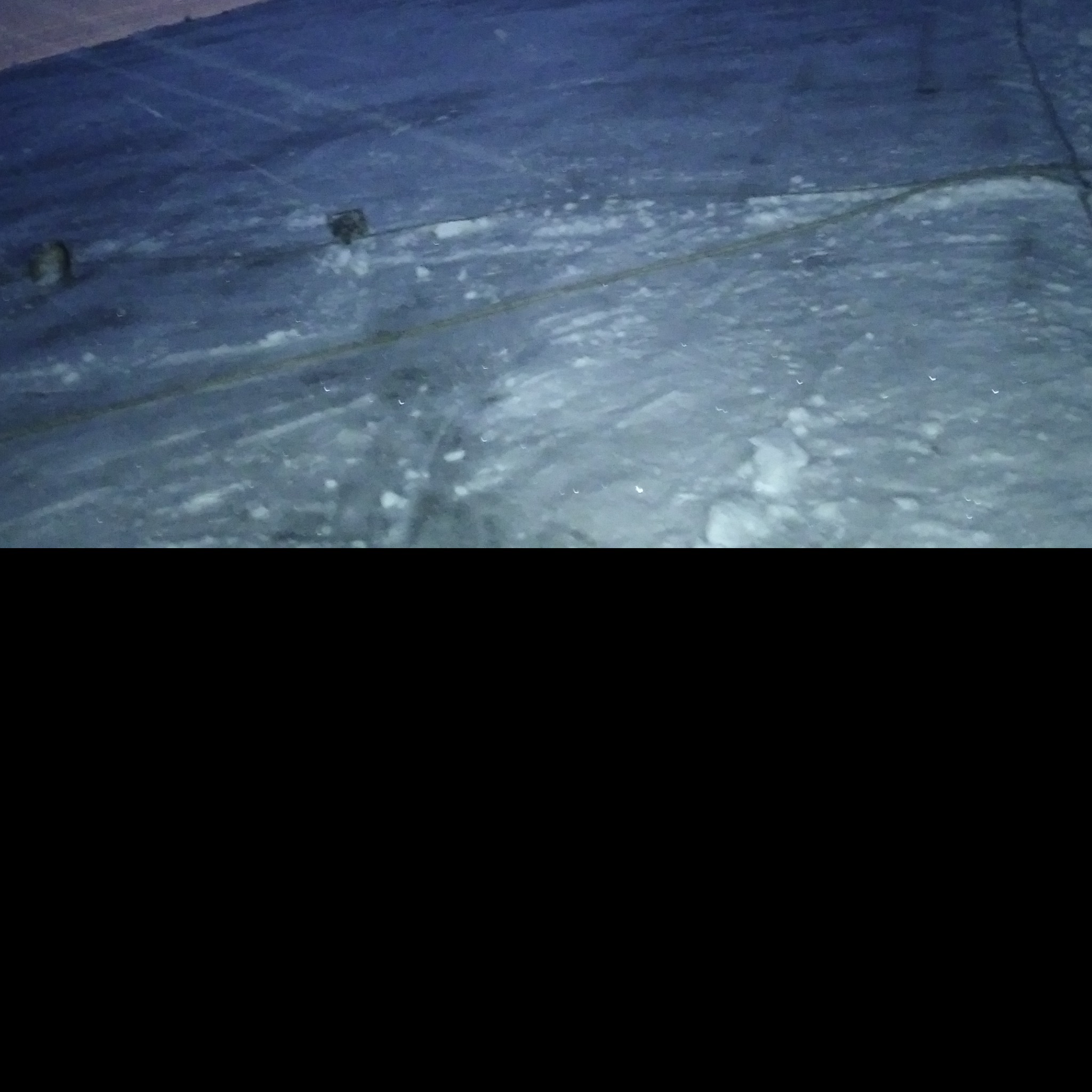 Zaśnieżony dach z widocznymi elementami konstrukcyjnymi i śladami po odśnieżaniu, wykonany w słabym oświetleniu.